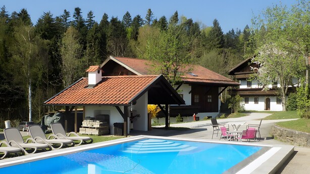 A poolside area with lounge chairs, a clear blue pool, and traditional wooden buildings with red-tiled roofs.