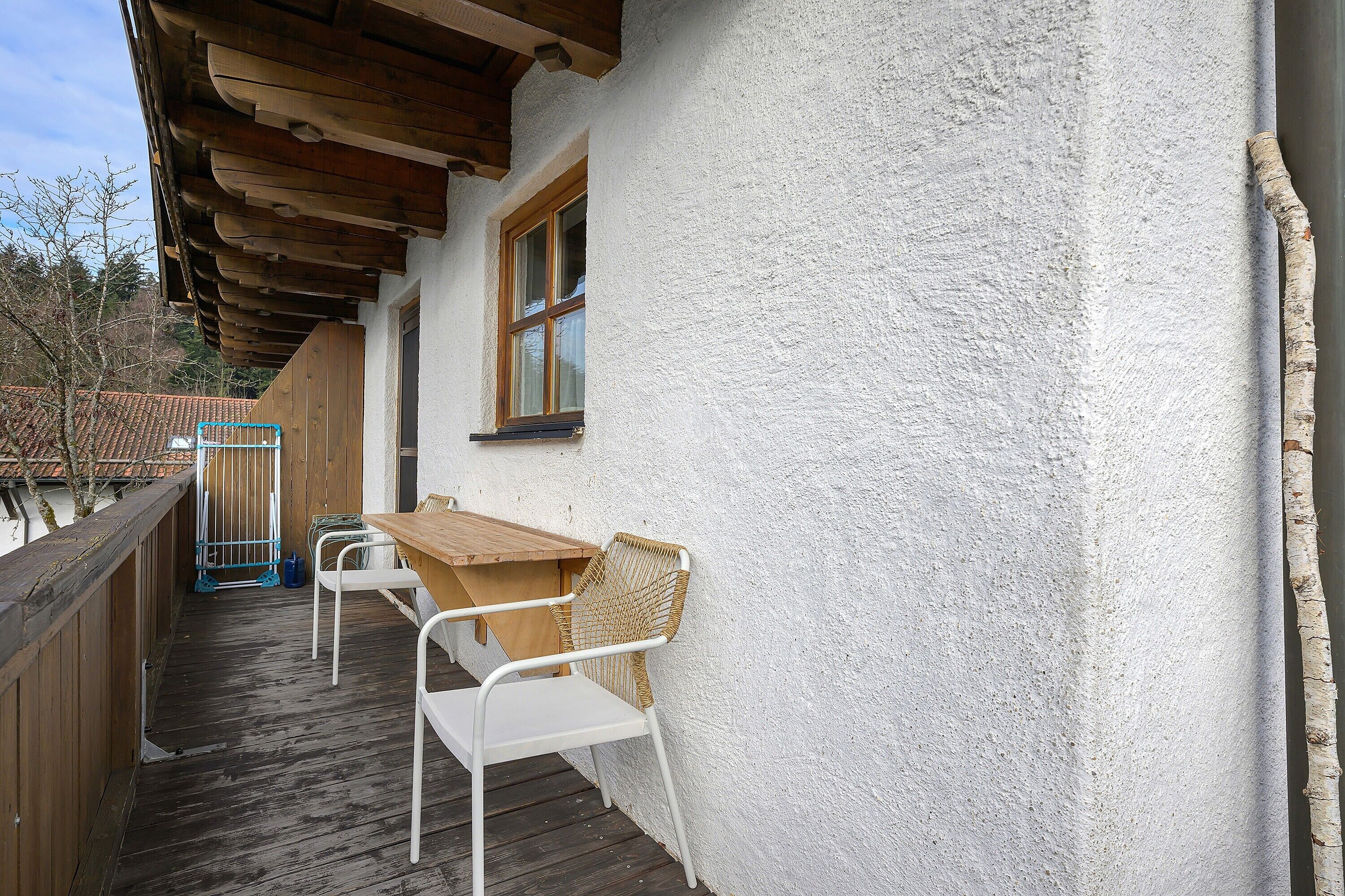 A wooden deck with a table and two chairs, a window, and a white wall.