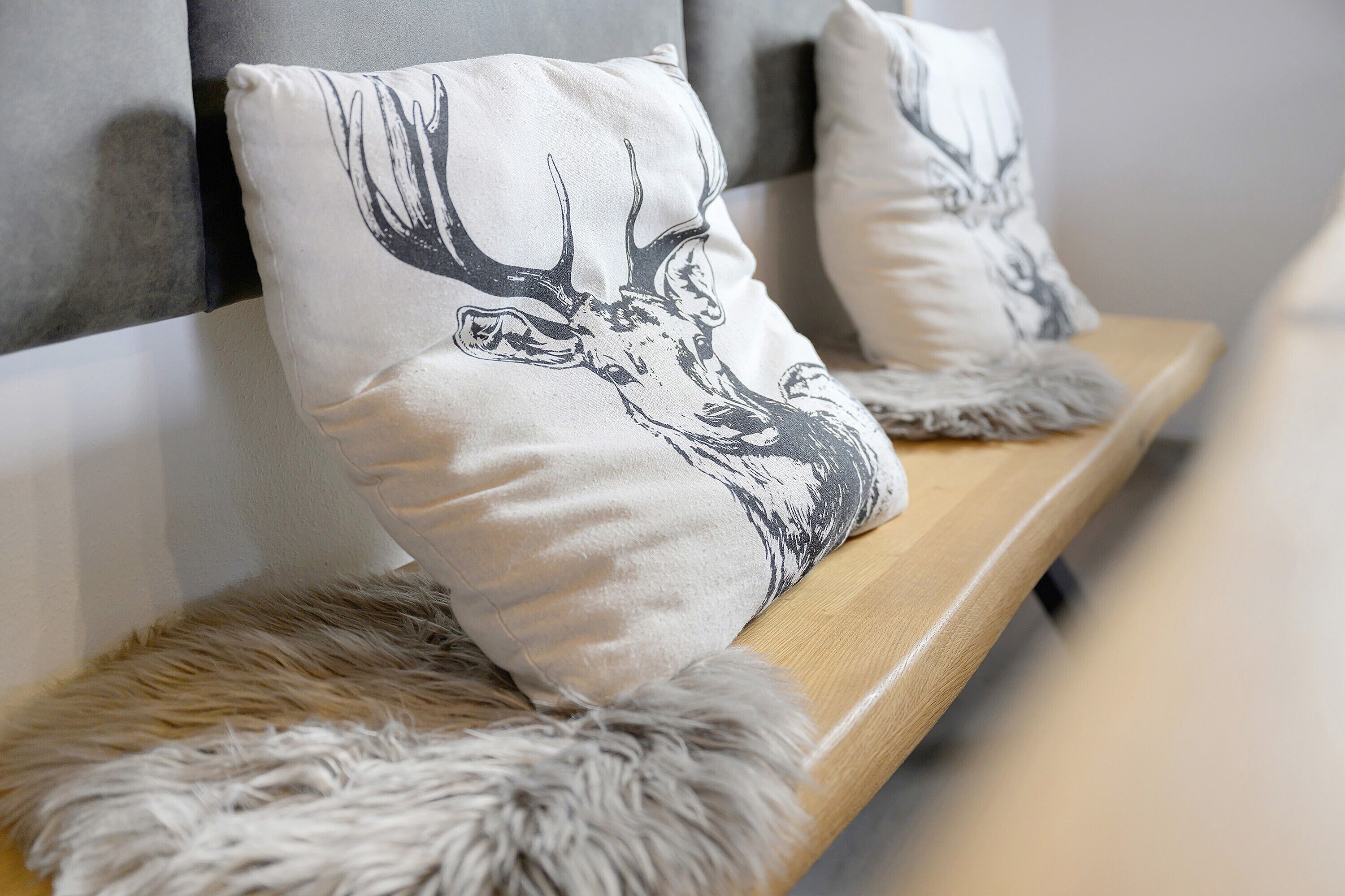 A bed with a white pillow featuring a deer design, a wooden headboard, and a fur throw.