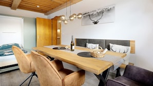 A modern room with a wooden ceiling, a dining table with chairs, a bed with a headboard, and a painting on the wall.
