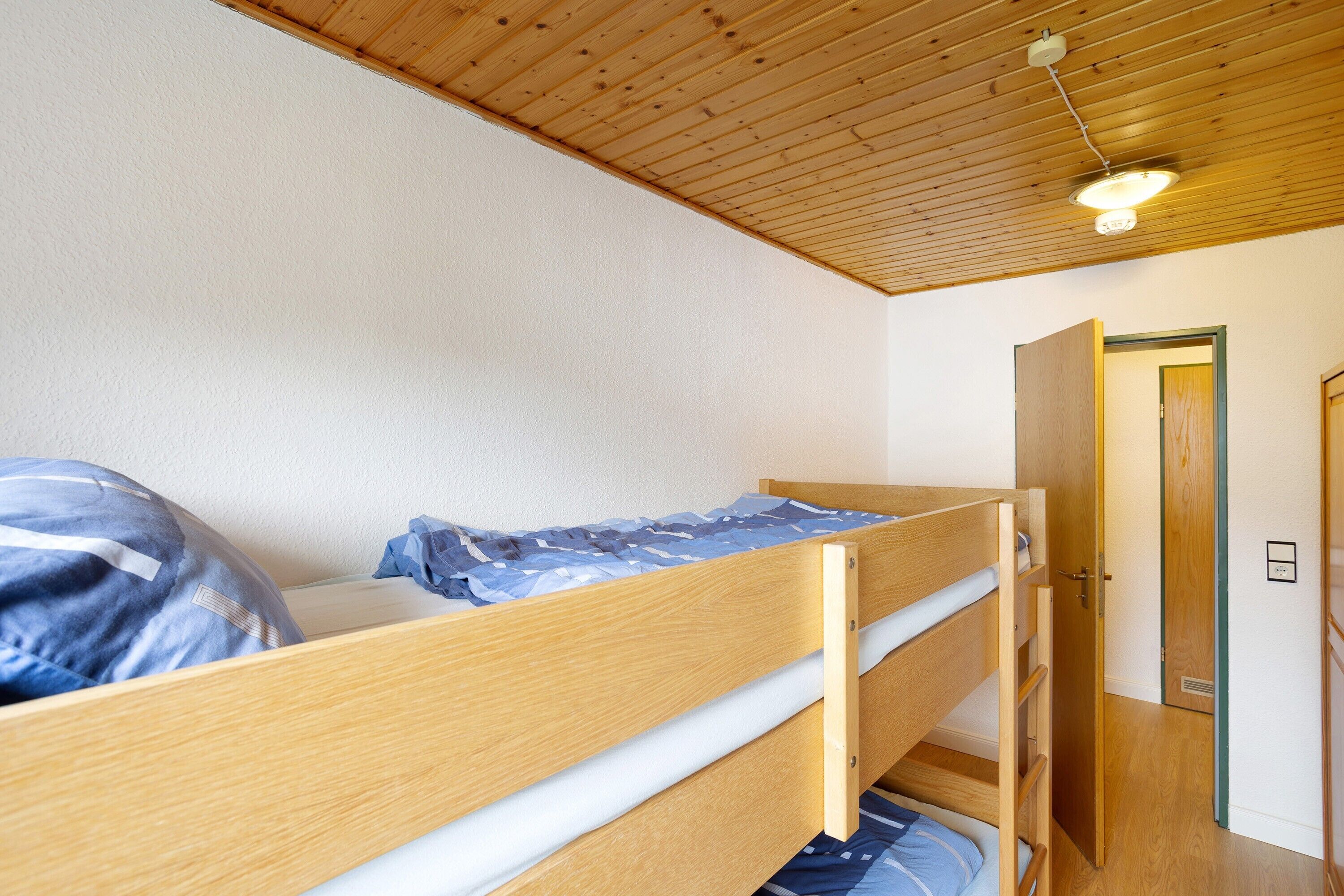Ein Stockbett mit Holzrahmen, einer ausziehbaren Schublade und einer Deckenleuchte.