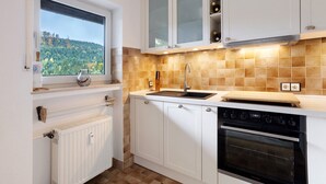 Una cocina con armarios blancos, una ventana con vistas, horno empotrado y salpicadero de azulejos.