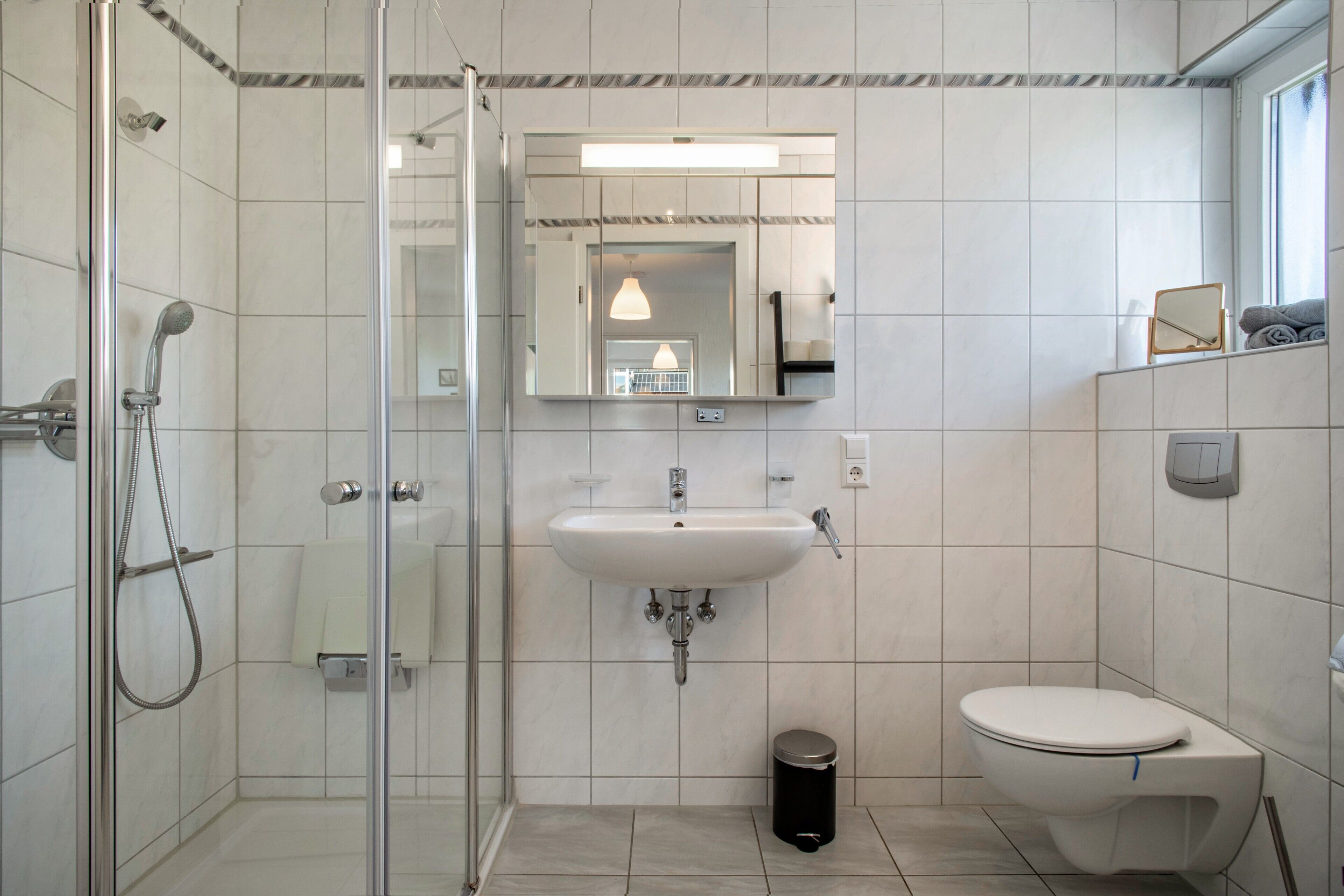 Een badkamer met een douchecabine van glas, een wastafel, een toilet en een spiegel.
