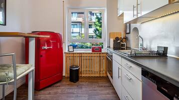 A compact kitchen with a red Bosch refrigerator, a Siemens dishwasher, and a window with a view of buildings.
