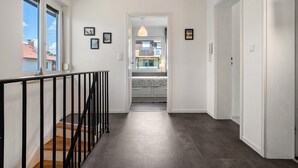 A hallway with a staircase, a door, and a view into a room with a bed and a hanging light fixture. - Casa Noho: Private Terrace, Garden, Wi-Fi – Lake Constance Retreat for Families & Friends (Nonnenhorn)