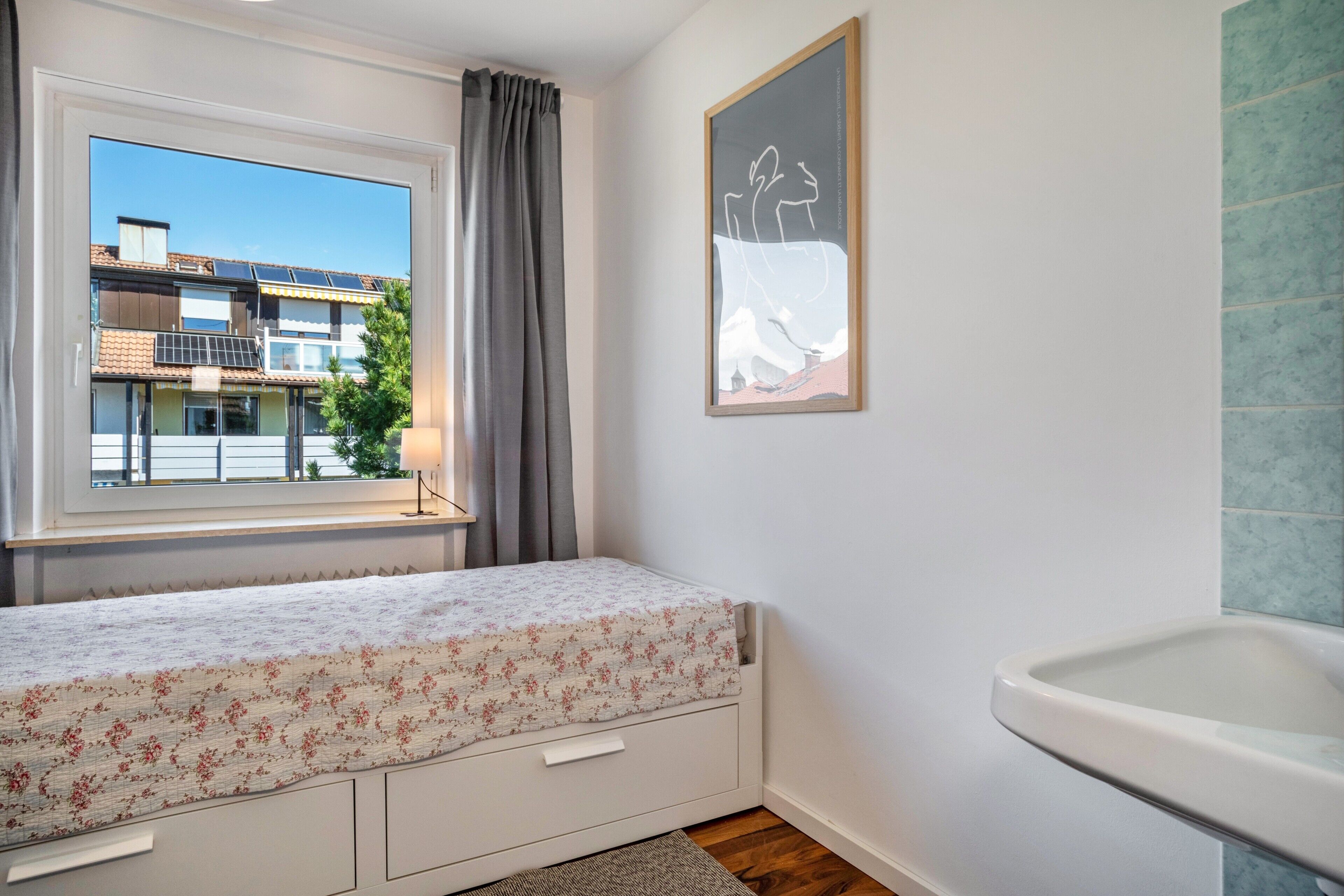 Ein Schlafzimmer mit Bett, Fenster, Badezimmer mit Waschbecken und einem gerahmten Bild an der Wand.
