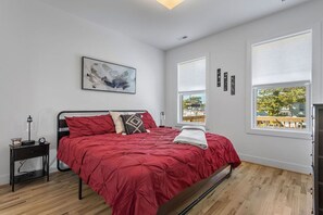 Ein Schlafzimmer mit einem Bett, einem Nachttisch, einem Fenster und einem Bild an der Wand.