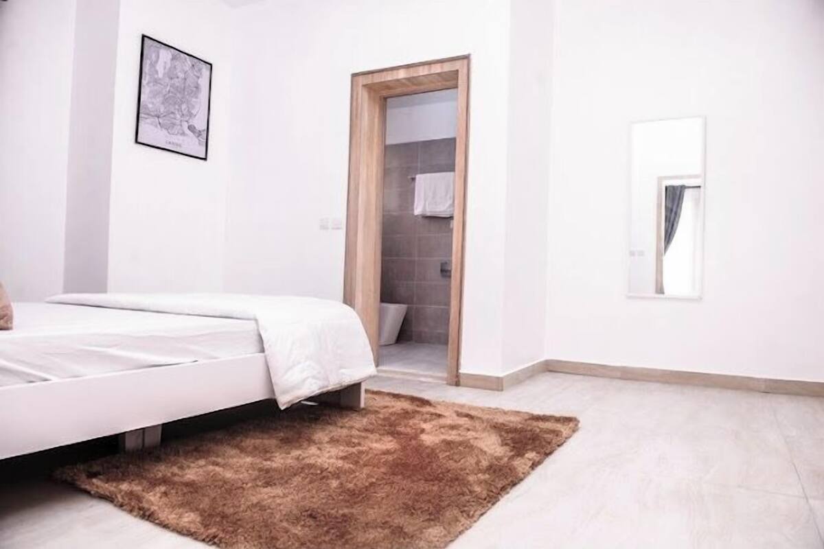 Ein Schlafzimmer mit einem Bett, einem braunen Teppich, einem gerahmten Bild an der Wand und einer Tür zu einem Badezimmer.