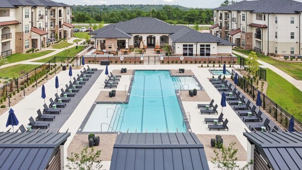Una piscina con sillones de descanso y sombrillas, rodeada de edificios de apartamentos.