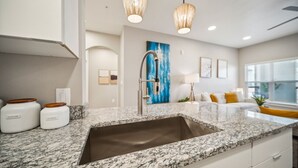 Una cocina moderna con encimeras de granito, un lavamanos de acero inoxidable e iluminación colgante.