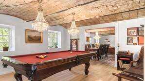A billiards table with a red cloth, wooden furniture, and chandeliers in a room with a brick ceiling.