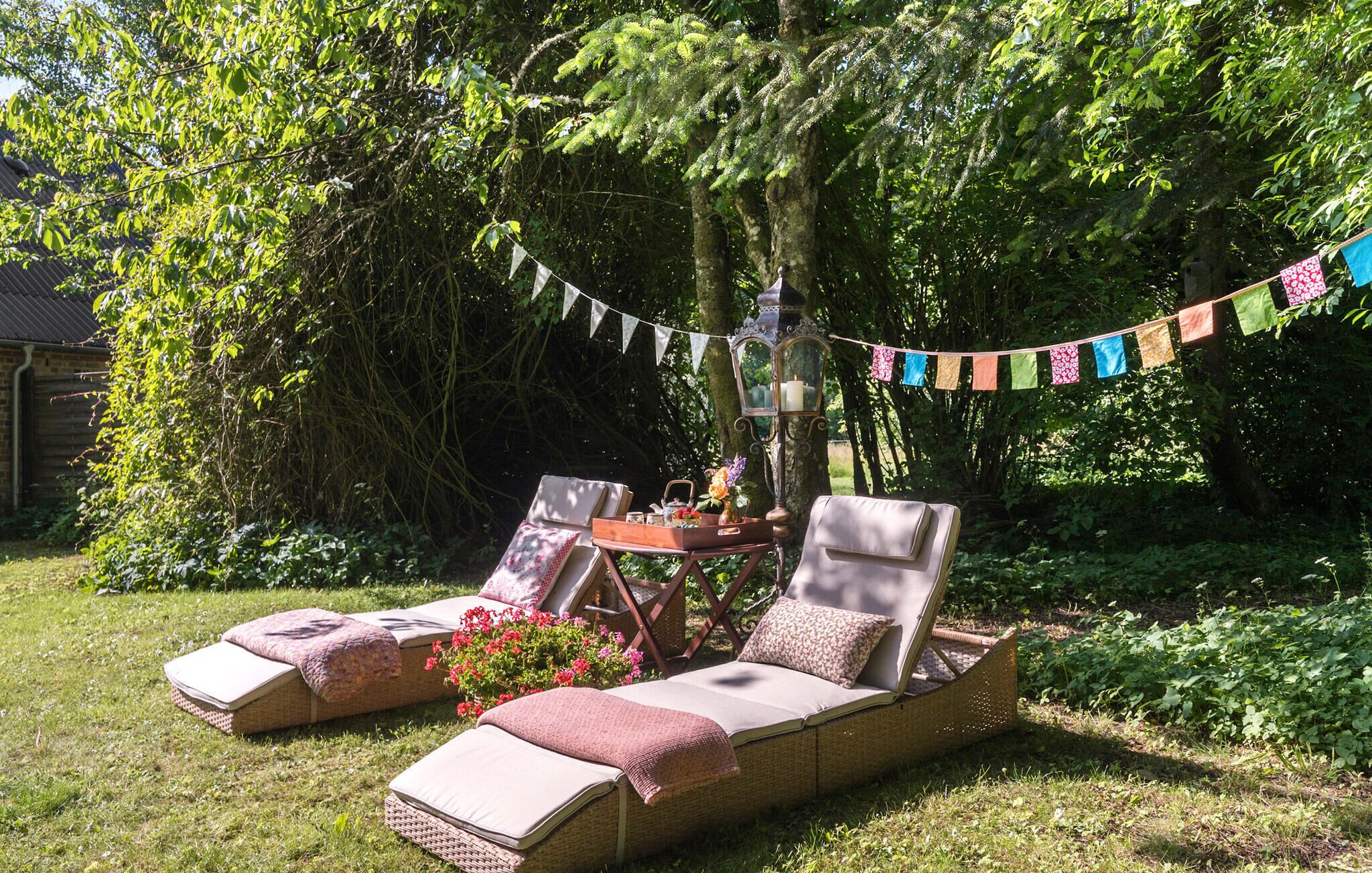 Two wicker lounge chairs with cushions, a small table with a candle and flowers, and a string of colorful flags.