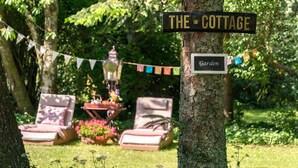 A sign reading "THE COTTAGE" and "Garden" in a lush, green outdoor setting with a picnic table and lounge chairs.