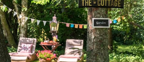 A sign reading "THE COTTAGE" and "Garden" in a lush, green outdoor setting with a picnic table and lounge chairs.