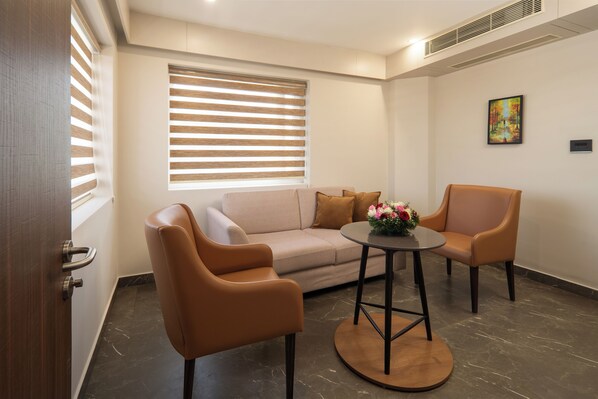 A modern living room with a sofa, two armchairs, a round table with a vase of flowers, and a painting on the wall.