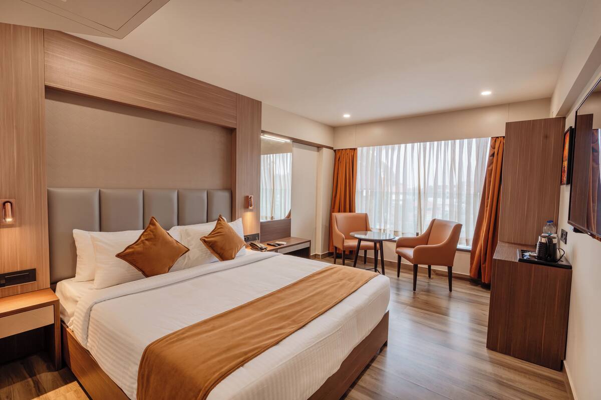 A hotel room with a large bed, a desk, a chair, a TV, and a window with curtains.
