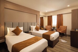 A hotel room with two beds, a desk, a chair, and a small table with a vase of flowers. - Classik Fort Inn and Suites (Kanayannur)