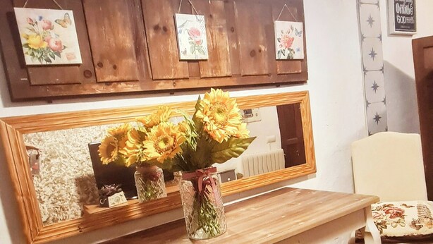 Una stanza con un tavolo di legno, uno specchio e un vaso di girasoli. Decorazioni a motivi stellari sulle pareti e una citazione incorniciata.