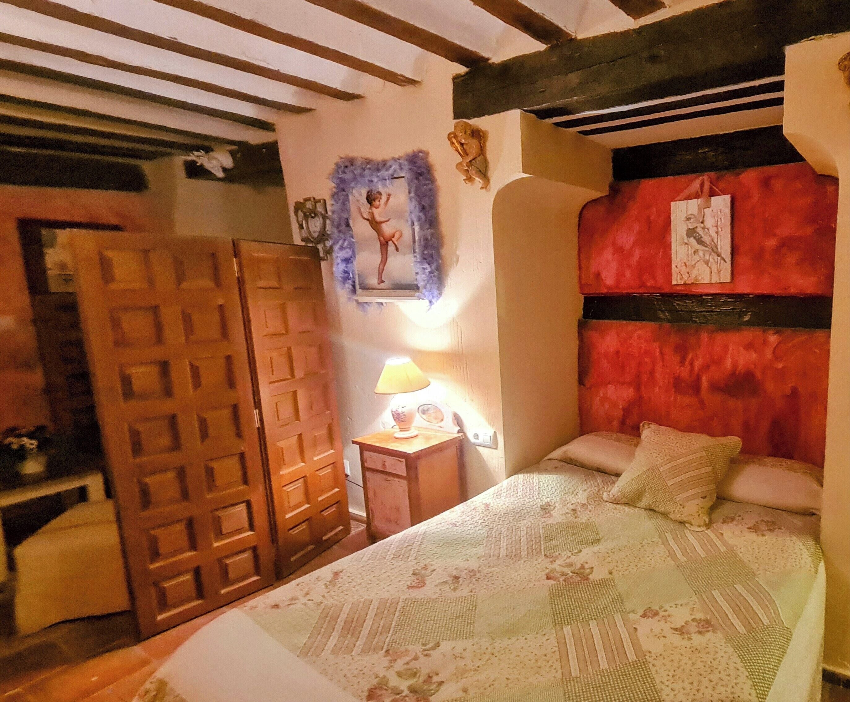 A bedroom with a bed, a nightstand, a lamp, a door, and a wall with a painting.