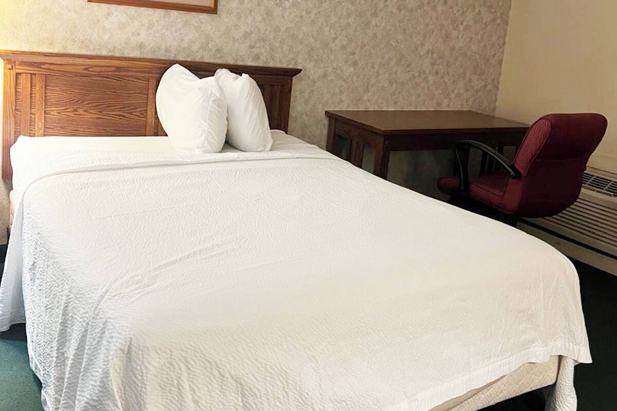 Ett hotellrum med en stor säng, en sänggavel i trä, ett litet bord, en röd stol och en inramad tavla på väggen.