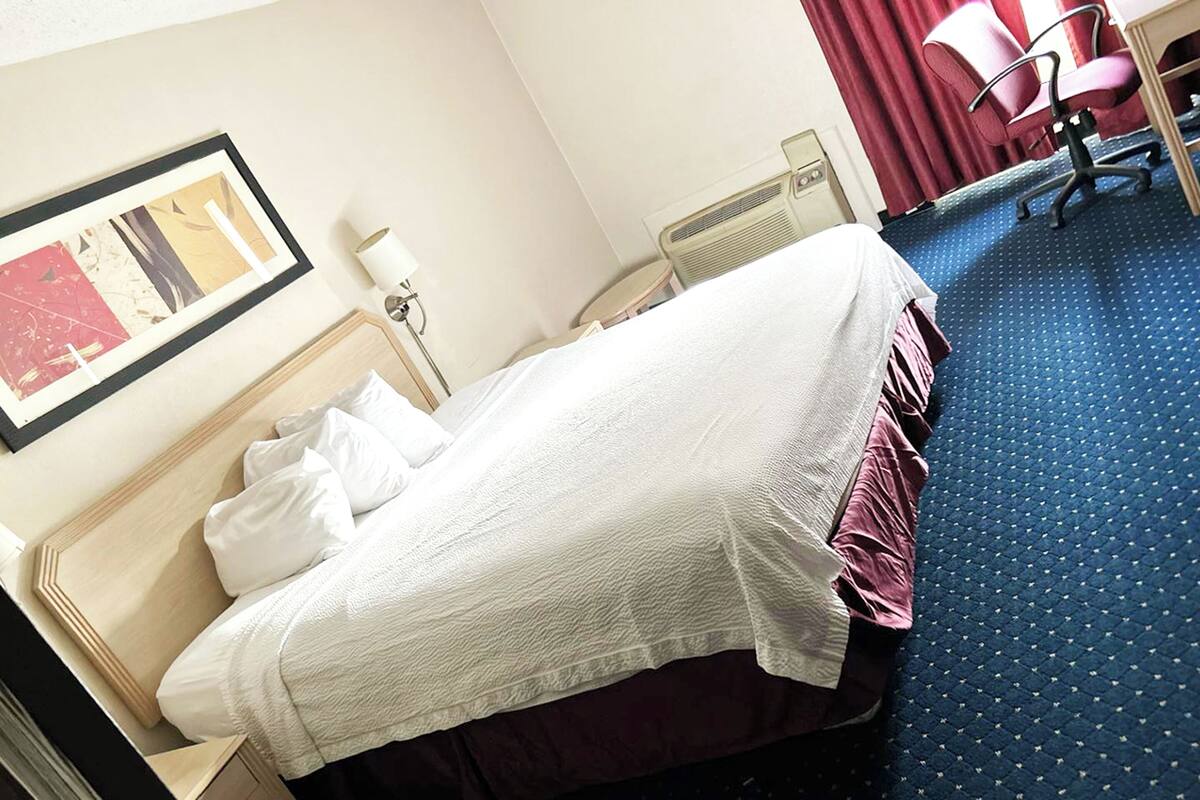 Ett hotellrum med en säng, ett skrivbord, en stol, ett element och en inramad tavla på väggen.