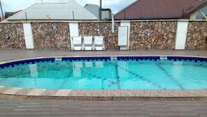 Una piscina con pared de piedra y borde de azulejos, rodeada por una cubierta de madera.