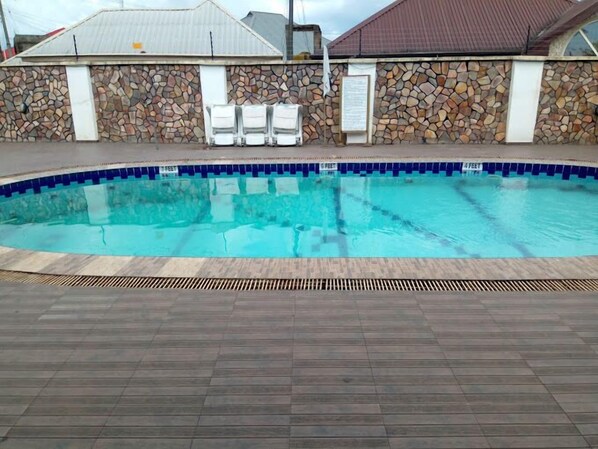 A swimming pool with a stone wall and a tiled edge, surrounded by a wooden deck. - EBIIS HOTEL (Yenagoa)
