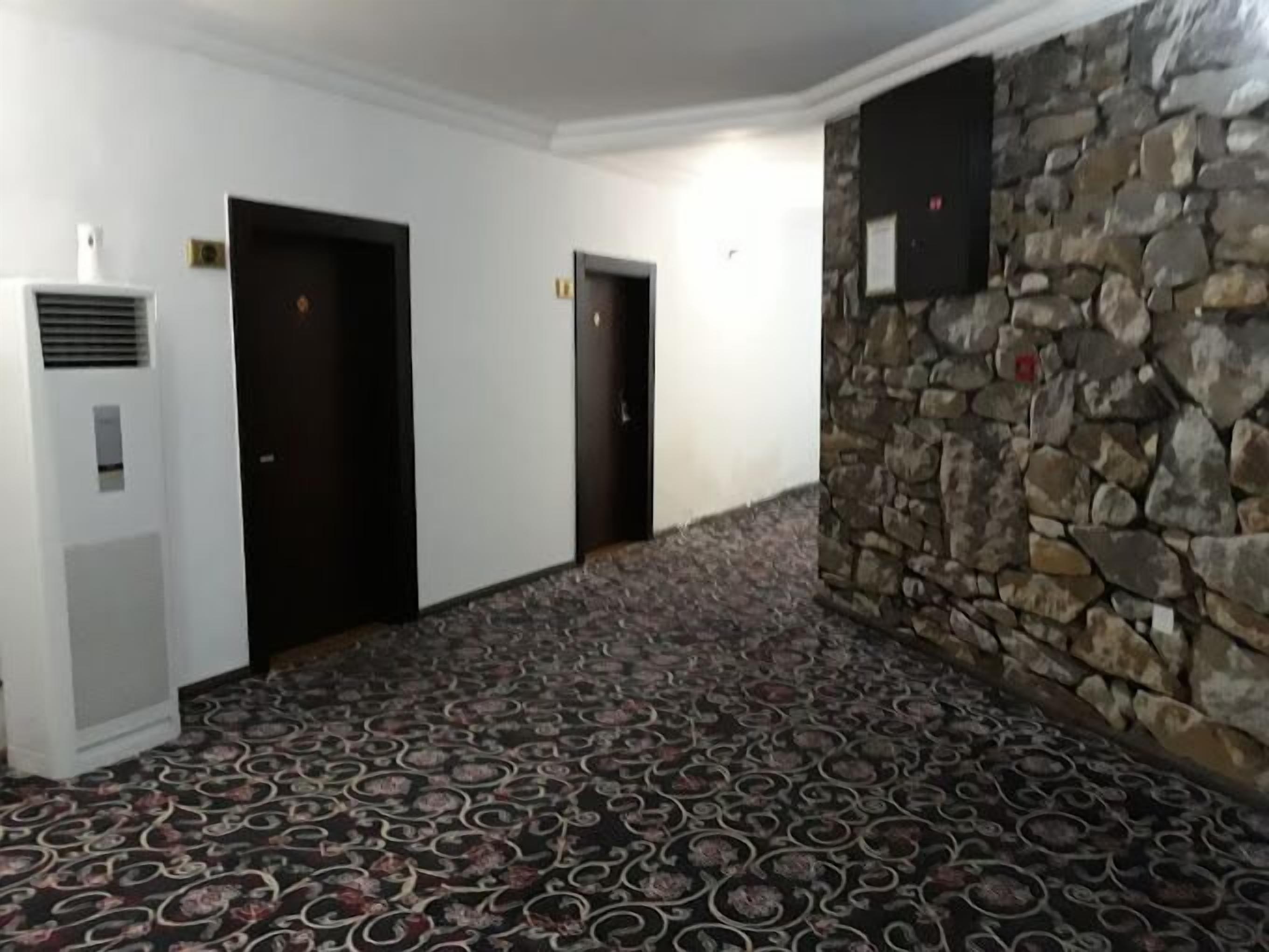 A hallway with patterned carpet, a stone wall, and three doors.