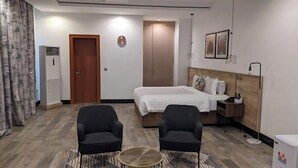 Habitación de hotel con cama, dos sillones, una mesita redonda, armario y un reloj en la pared.