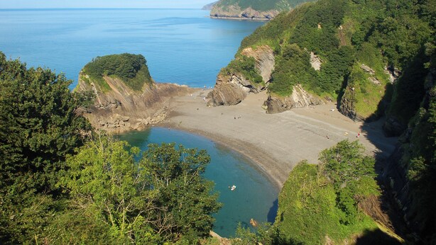 A coastal landscape with a beach, cliffs, and a body of water. - Daisy Cottage Berrynarbor near Broadsands beach (Berrynarbor)