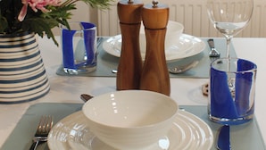 A dining table set with plates, bowls, cutlery, and a vase of flowers. - Daisy Cottage Berrynarbor near Broadsands beach (Berrynarbor)