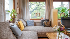 Ein modernes Wohnzimmer mit einer Eckcouch, einem Holztisch und Blick auf einen Baum durch große Fenster.