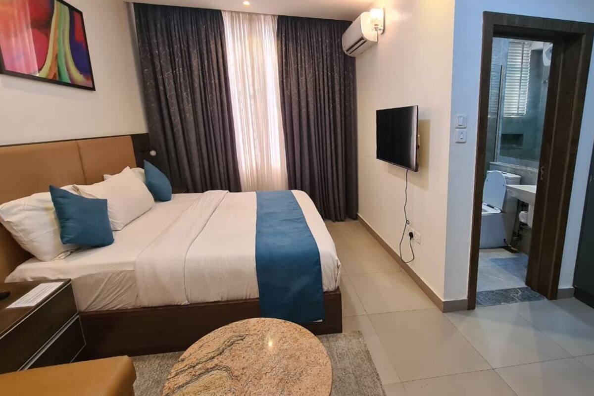 A hotel room with a bed, a TV, a desk, and a bathroom visible through an open door.