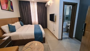 Een hotelkamer met een bed, een televisie, een bureau en een badkamer die door een open deur zichtbaar is.
