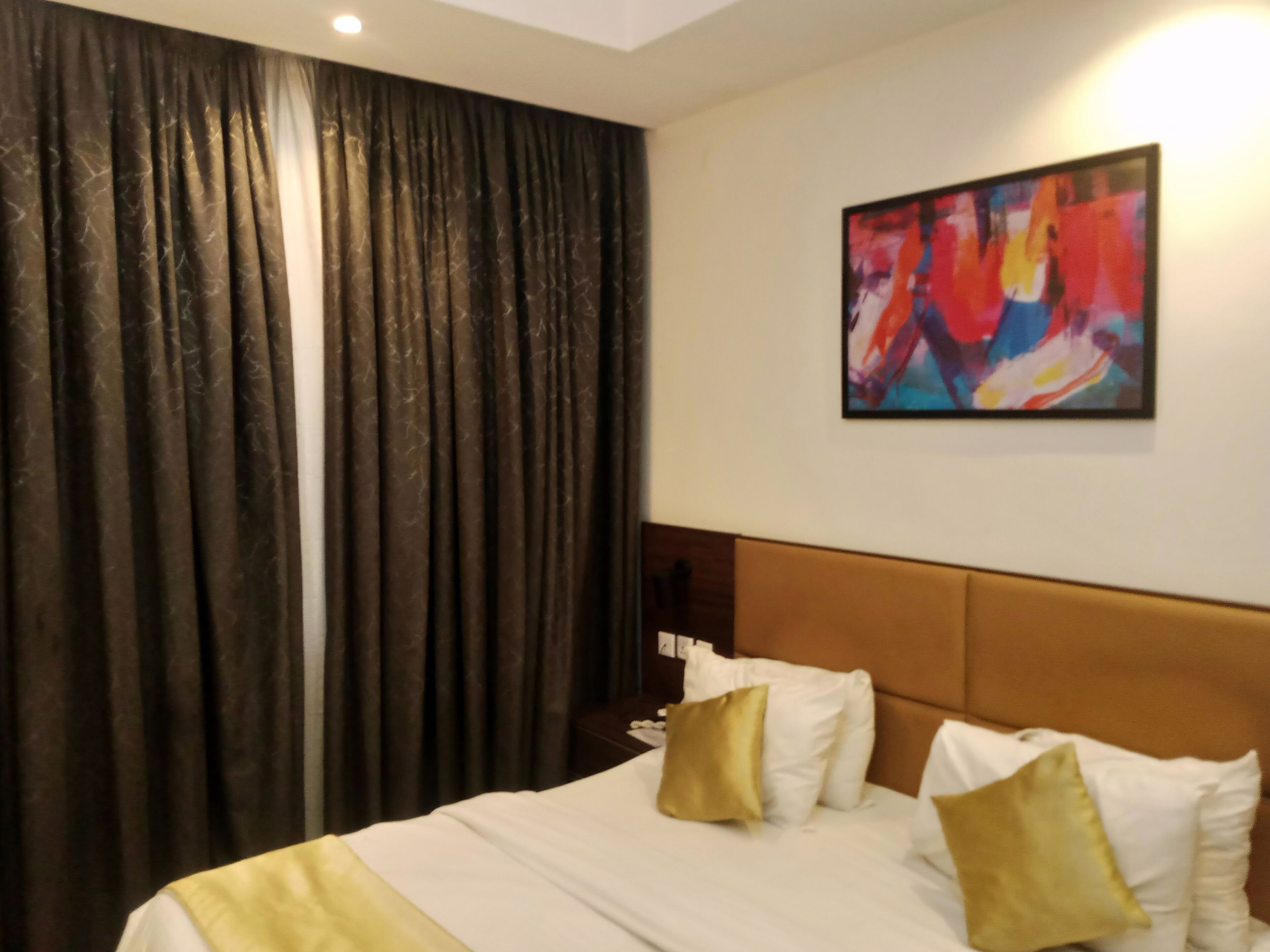 Une chambre d’hôtel avec un grand lit, une tête de lit, un tableau au mur et un rideau.