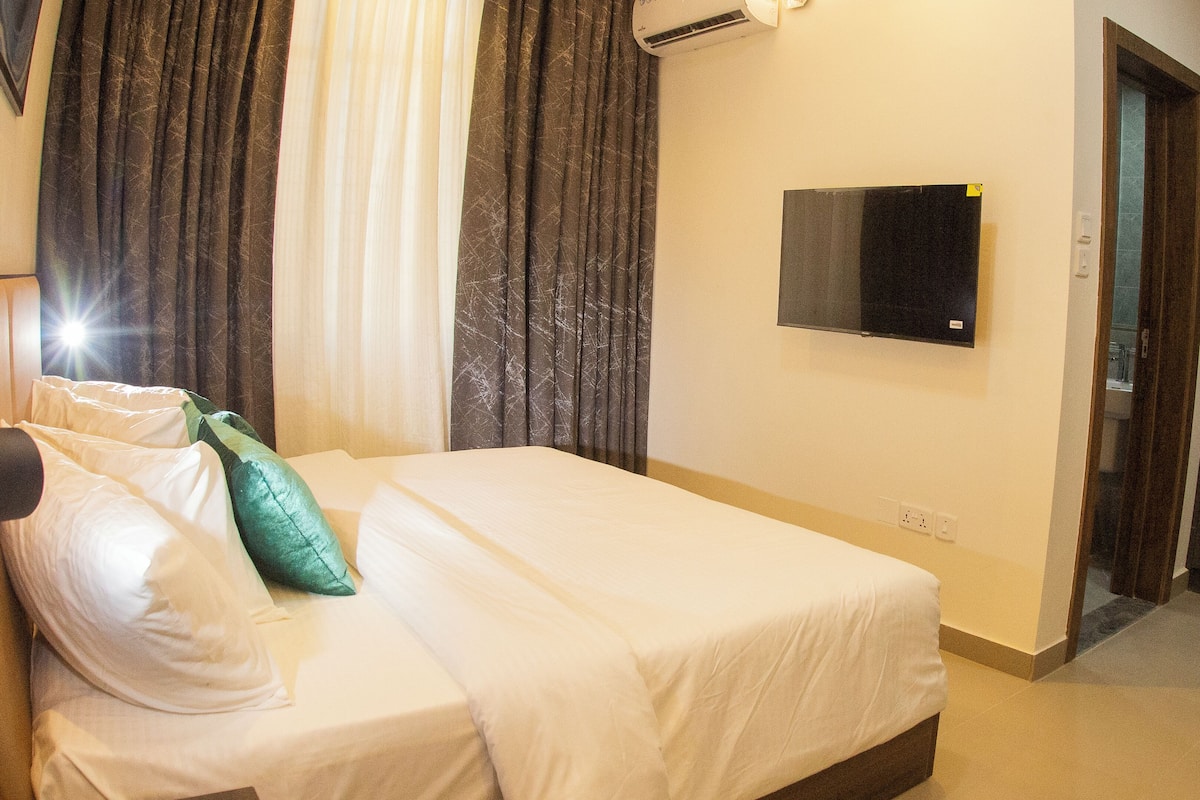 A hotel room with a bed, a television mounted on the wall, and a door leading to another room.