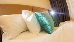 Ein Bett mit weißen und türkisfarbenen Kissen, einem Kopfteil und einem Vorhang.
