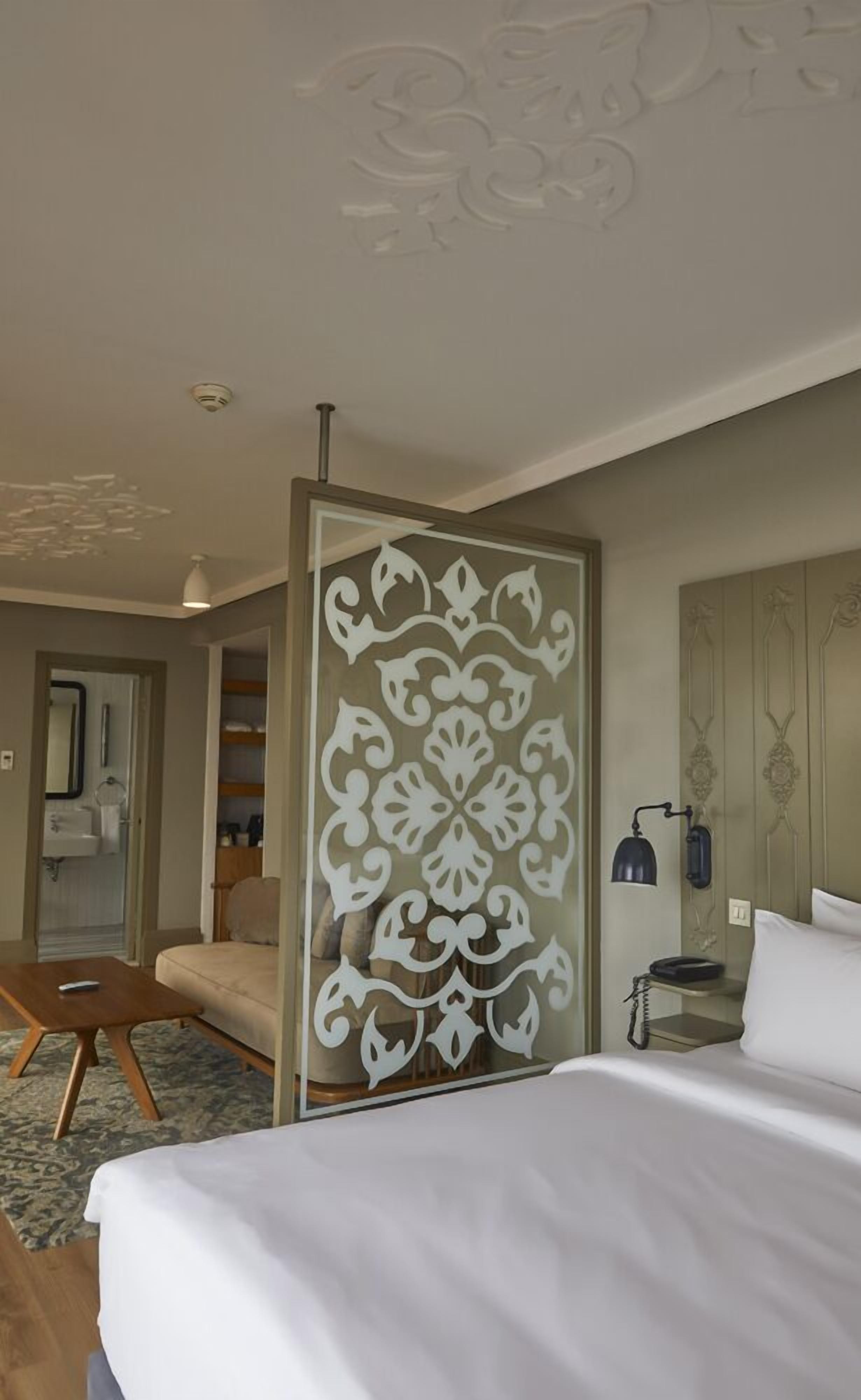 A hotel room with a bed, a sofa, a desk, and a decorative partition with a floral pattern.