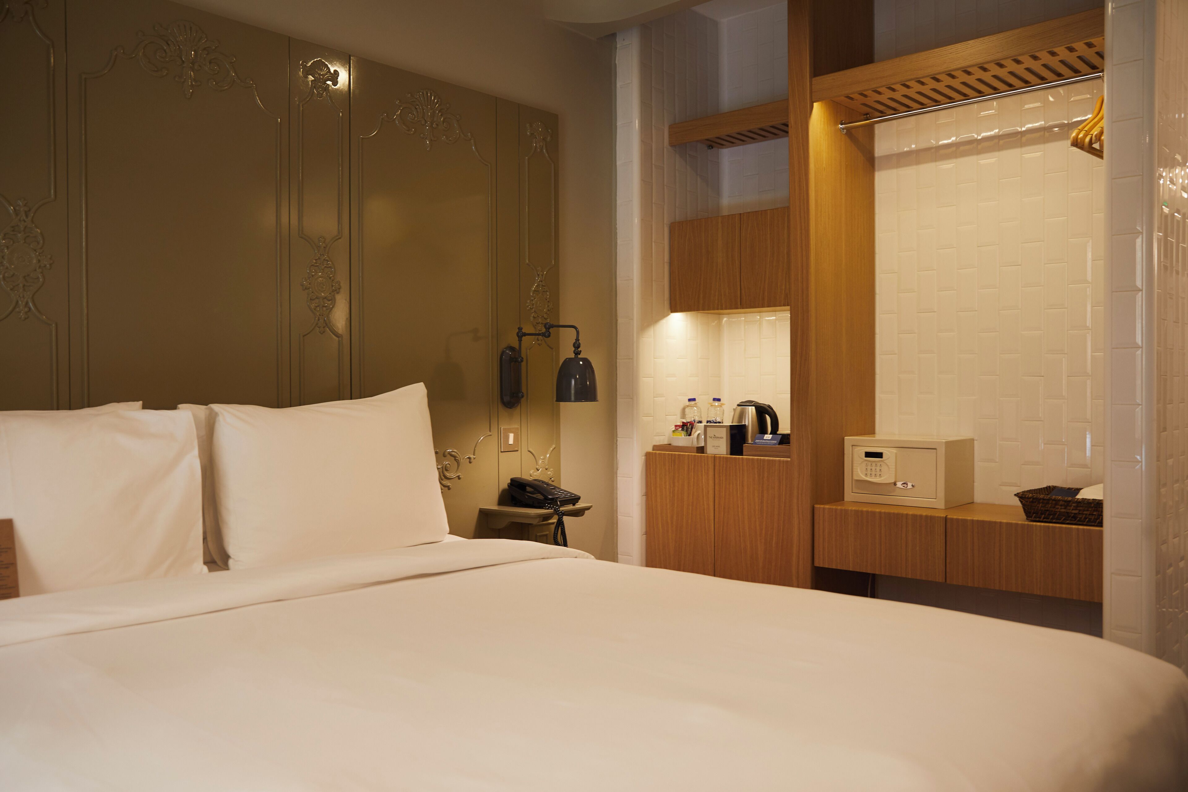 Habitación de hotel con una cama grande, una mesita de noche con lámpara, un armario de madera y un microondas.