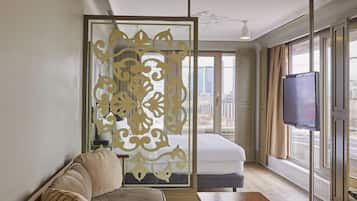 A modern hotel room with a sofa, a small table, a TV, and a decorative partition.