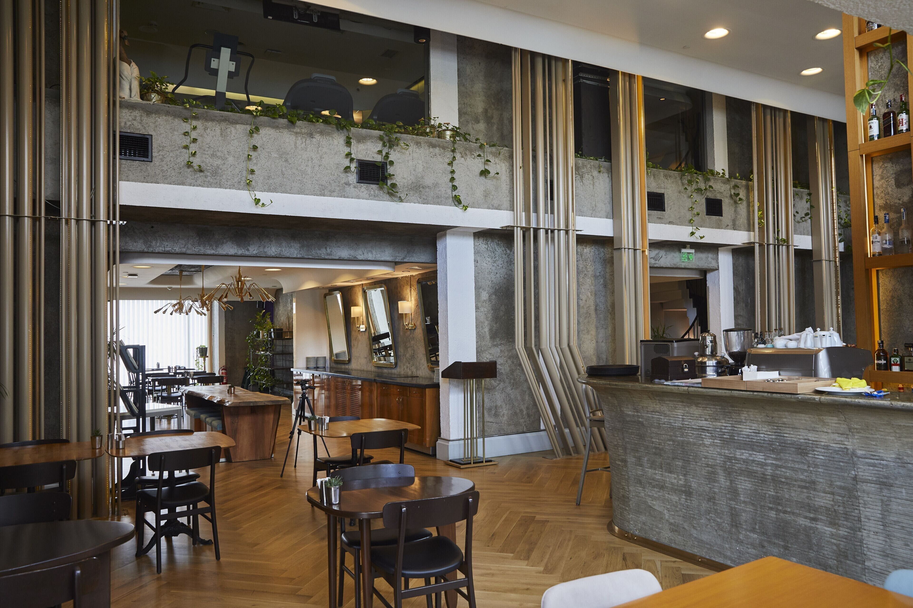 A modern restaurant with a high ceiling, wooden flooring, and a bar area.
