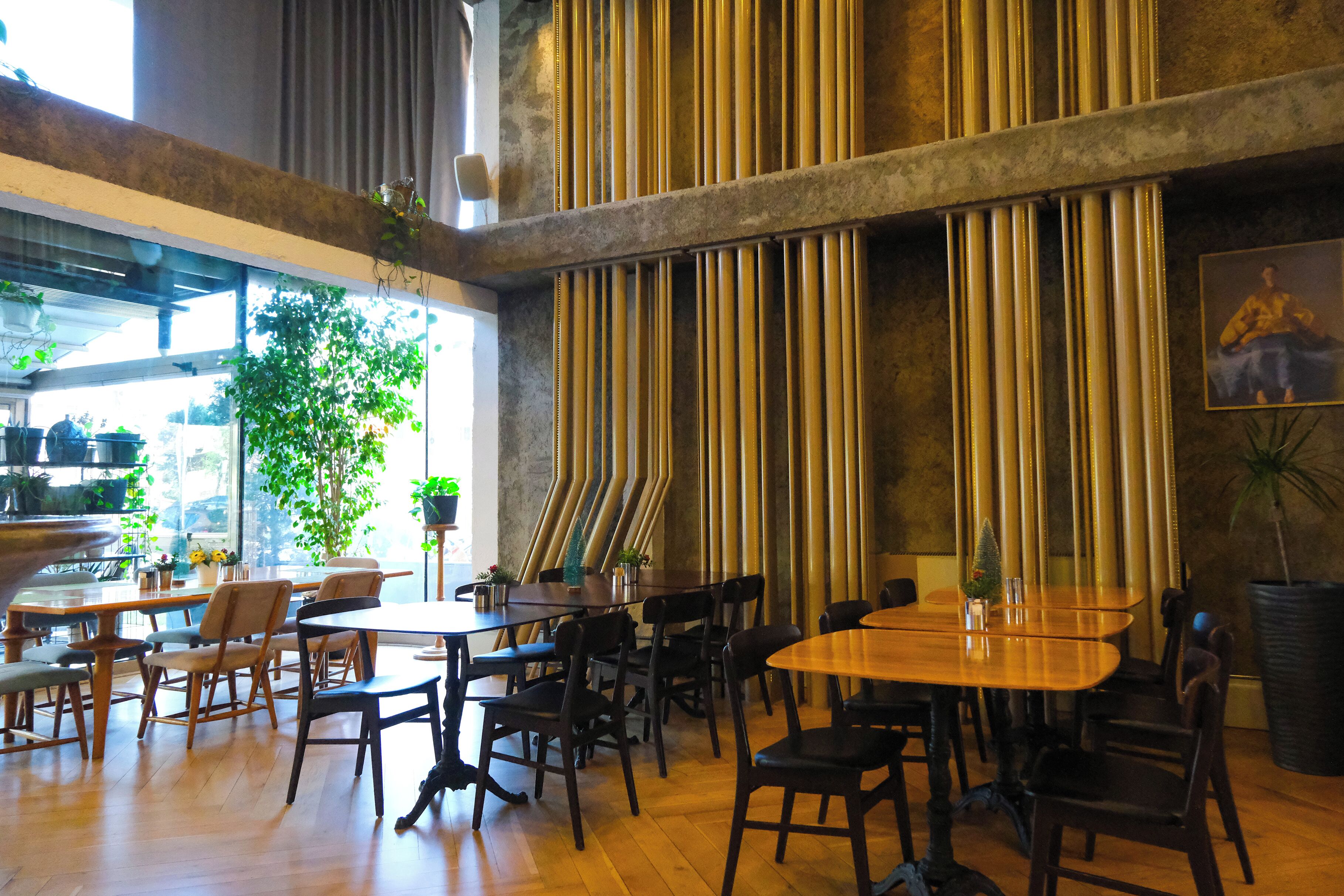 Een ruime, overdekte eetruimte met houten tafels en stoelen, grote ramen en verticale jaloezieën.