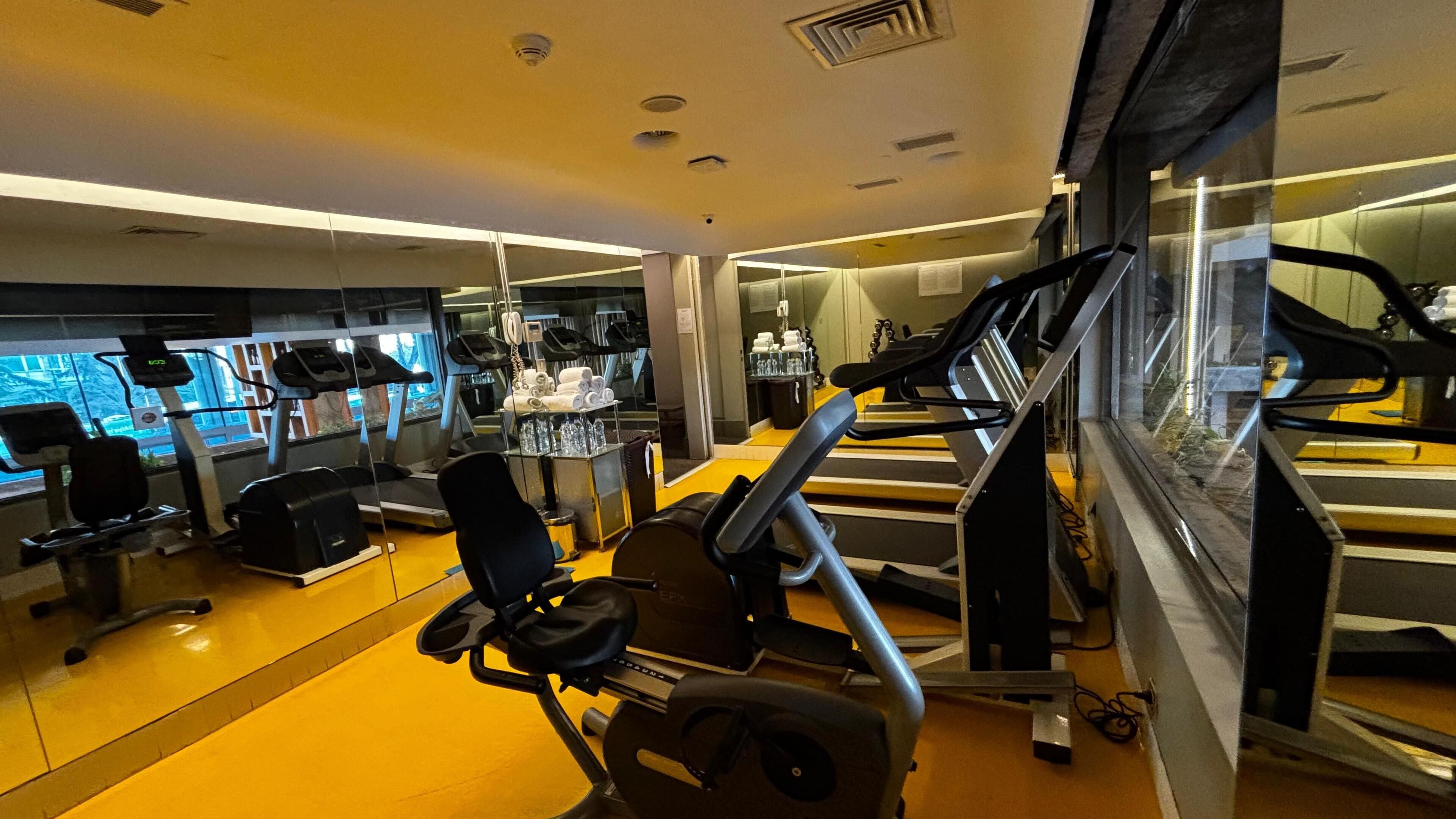A modern gym with cardio equipment, mirrors, and a yellow floor.
