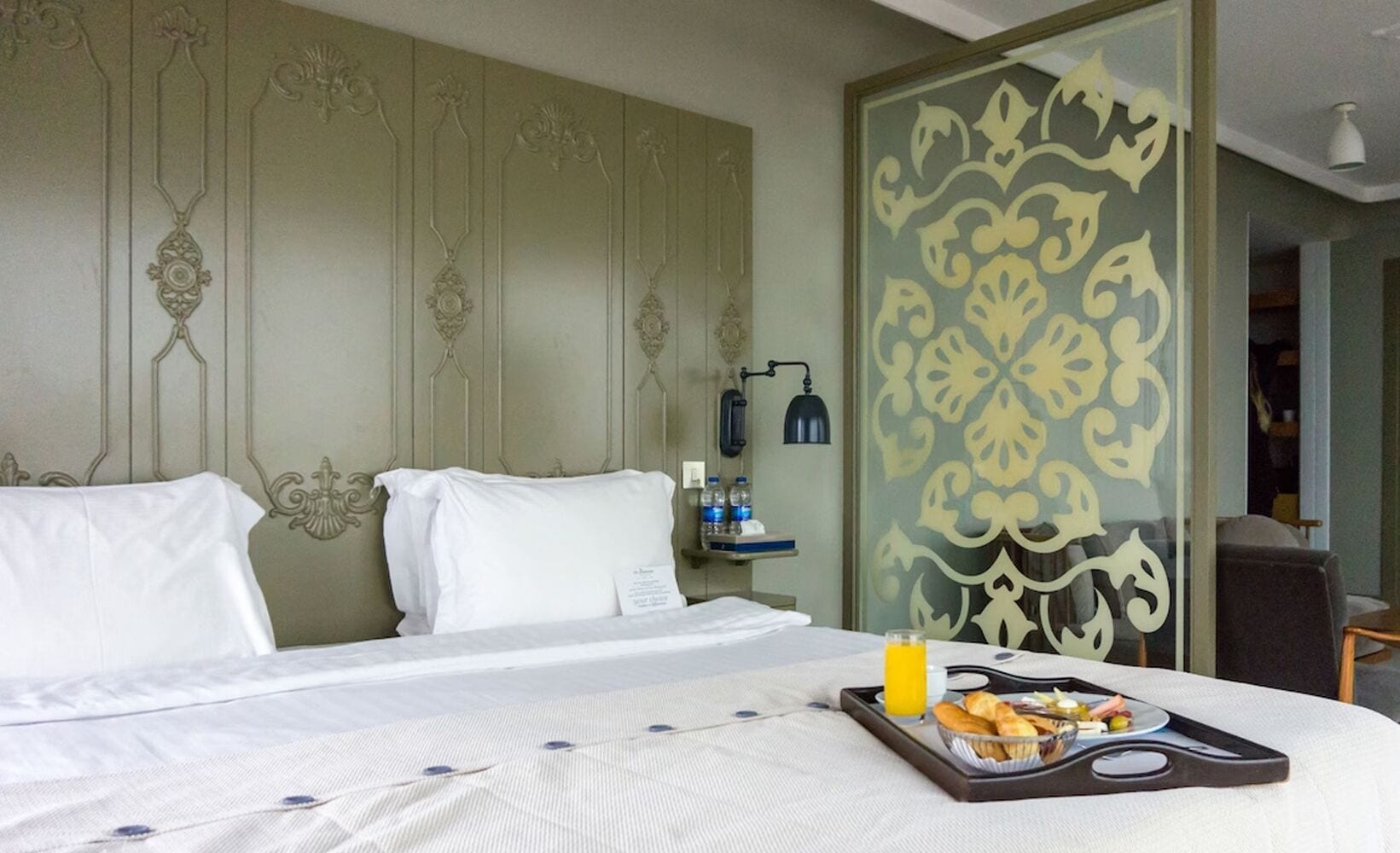 A hotel room with a neatly made bed, a tray with breakfast items, and a decorative wall panel.