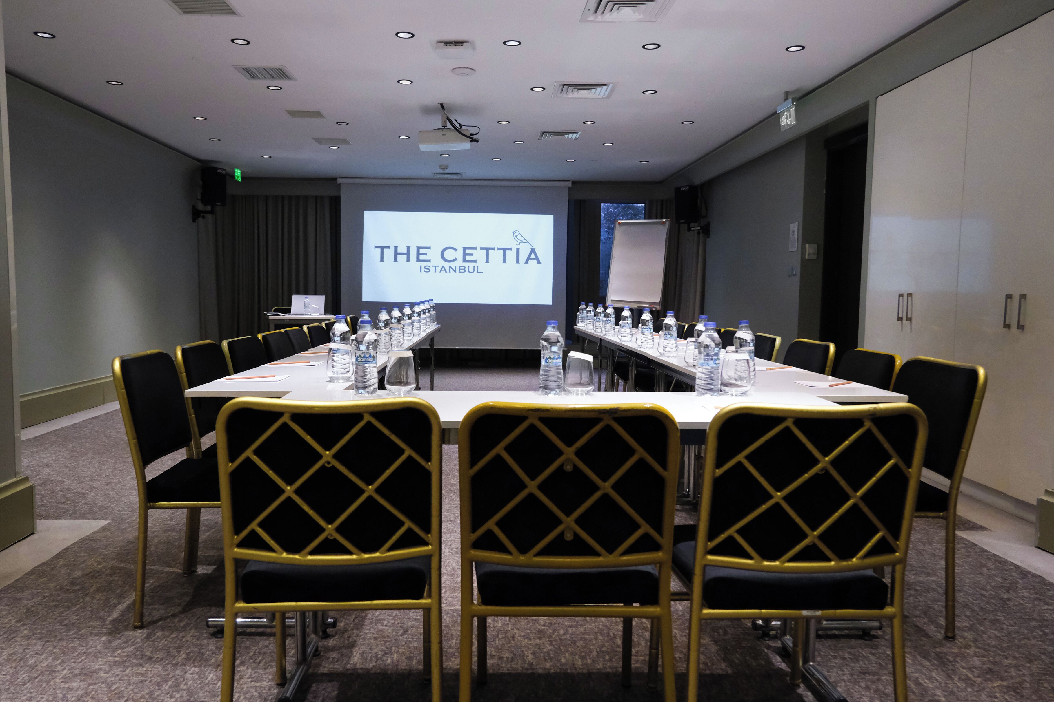 A conference room with a long table, yellow chairs, water bottles, and a presentation screen displaying "THE CETTIA ISTANBUL".