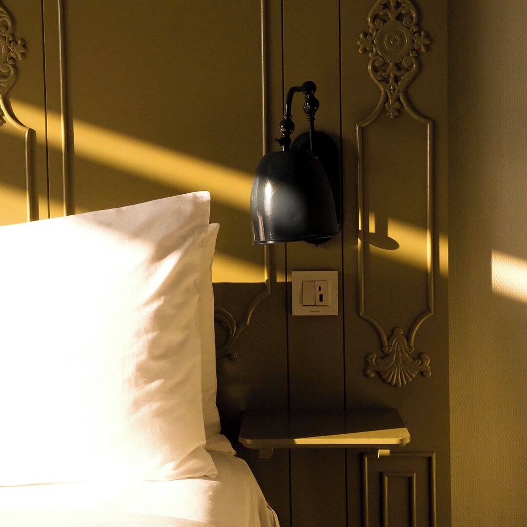 A bed with a white pillow and a black lamp on a wall with decorative moldings.