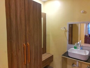 A bathroom with a wooden wardrobe, a sink with a mirror, and toiletries.
