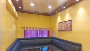 A living room with a sectional sofa, a small wooden coffee table, and a window with curtains. - Hotel Shobha (Forbesganj)