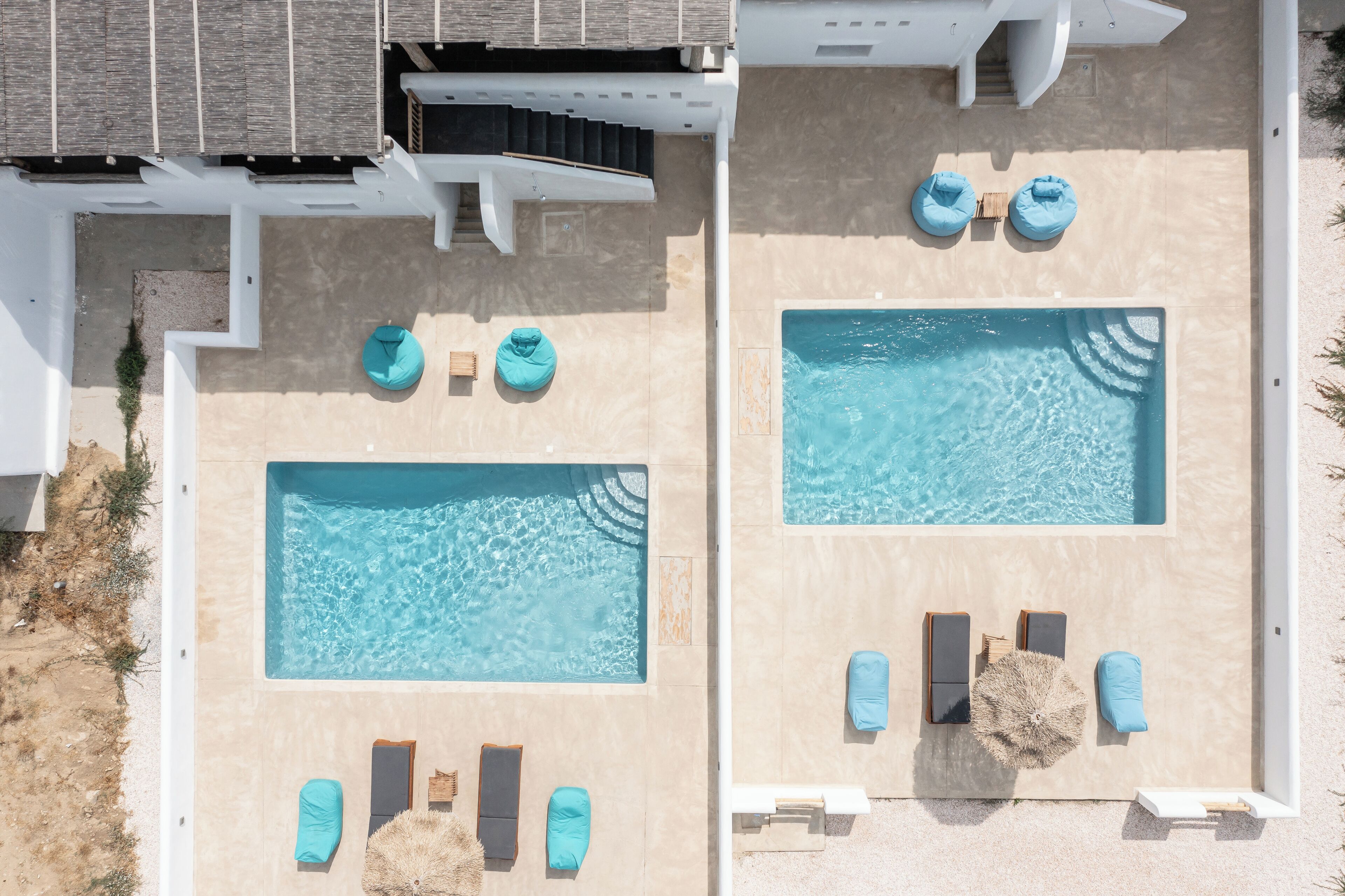 Zwei Swimmingpools mit Liegestühlen und Handtüchern, umgeben von einem weißen Gebäude mit Fliesenveranda.