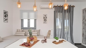 A modern living room with a large white sofa, a wooden coffee table with fruits and a pineapple, and a hanging light fixture. - White Cocoon Exclusive villas (Naxos)